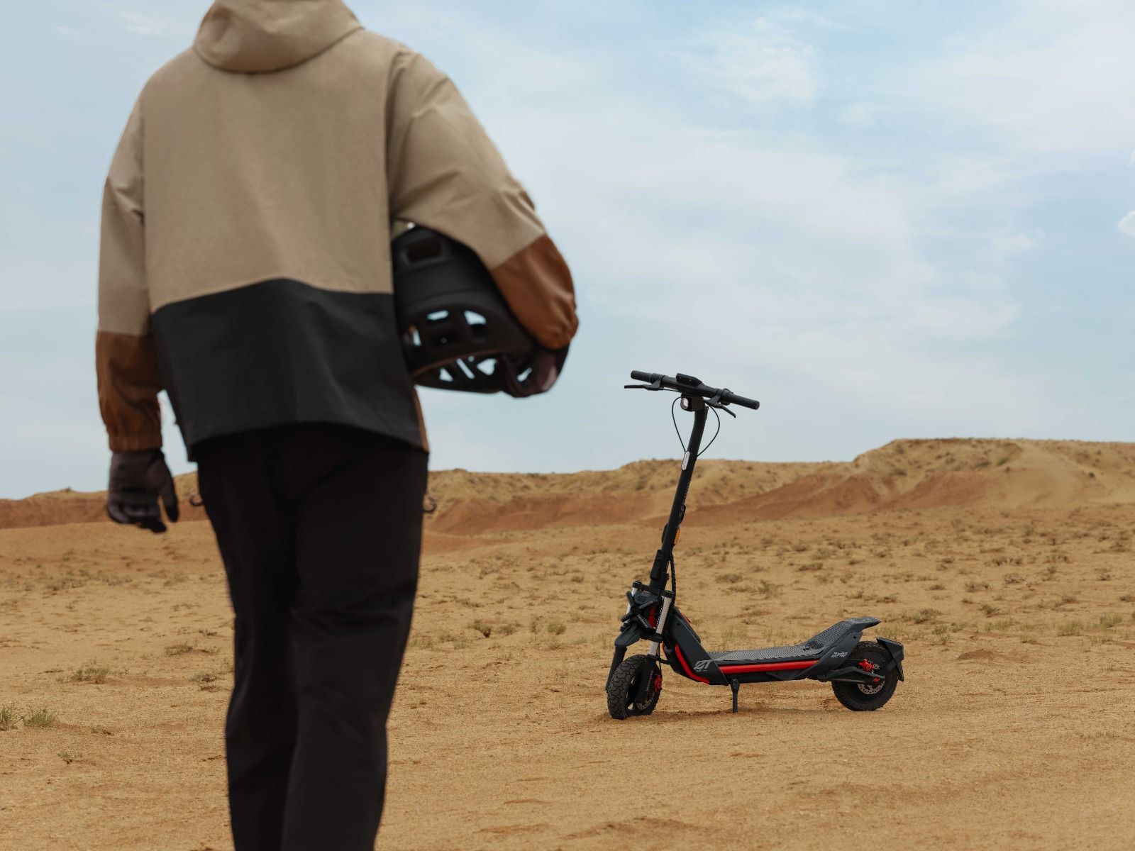 A person in a jacket, helmet in hand, strides toward a parked Segway ZT3 Pro in the desert landscape, poised to embrace off-road dominance.