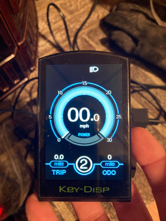 A close-up of the display model LCD Display for Sondors Ebikes shows 0.0 mph, 0.0 miles trip, and 2 miles on the odometer. The screen features a central gauge and the word "Key-Disp" at the bottom, typical of Sonders' easy installation design.