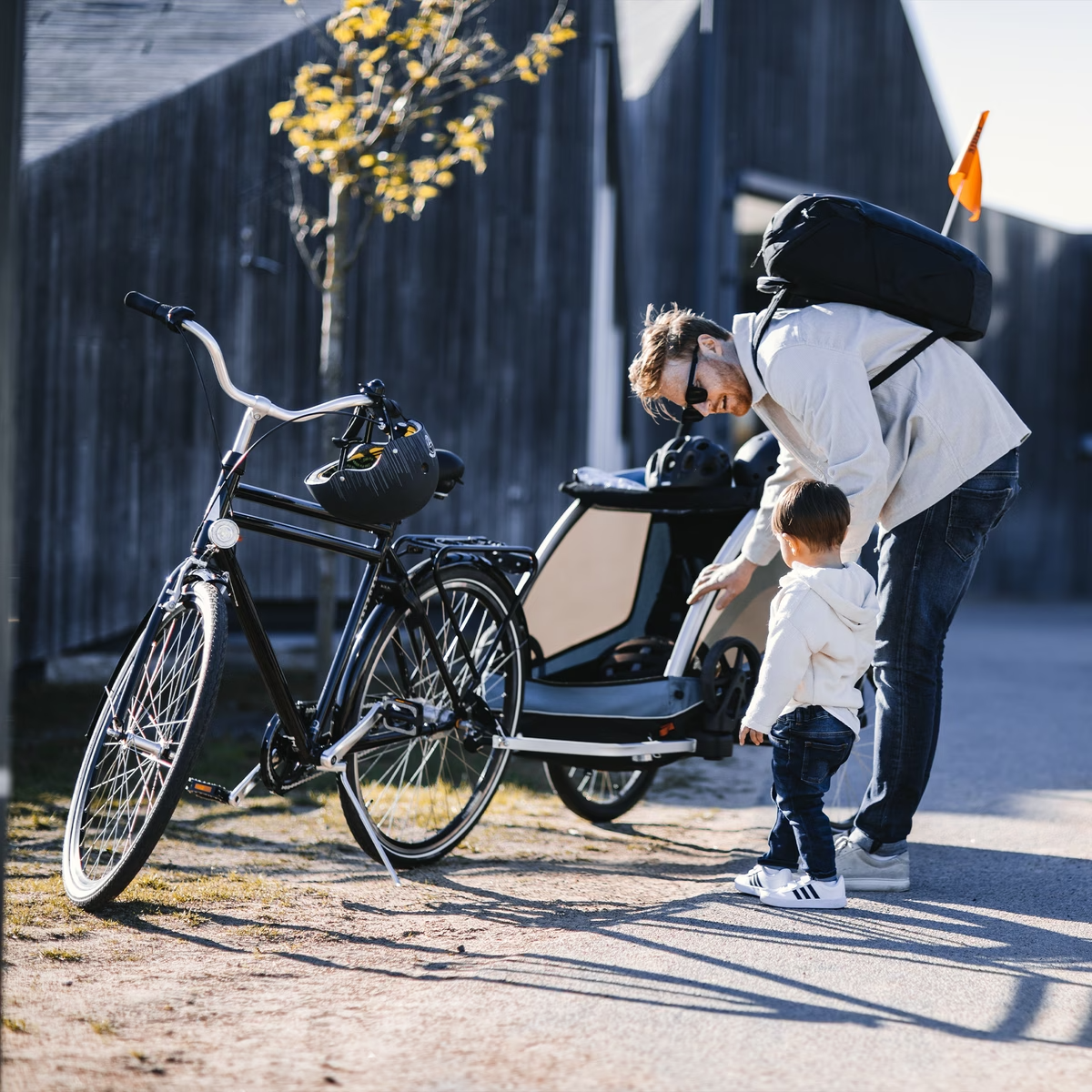 An adult assists a child with attaching the Thule Courier Child Trailer near a parked bike. Both are dressed casually, and it appears to be a sunny day in a residential area, making it perfect for family outings.