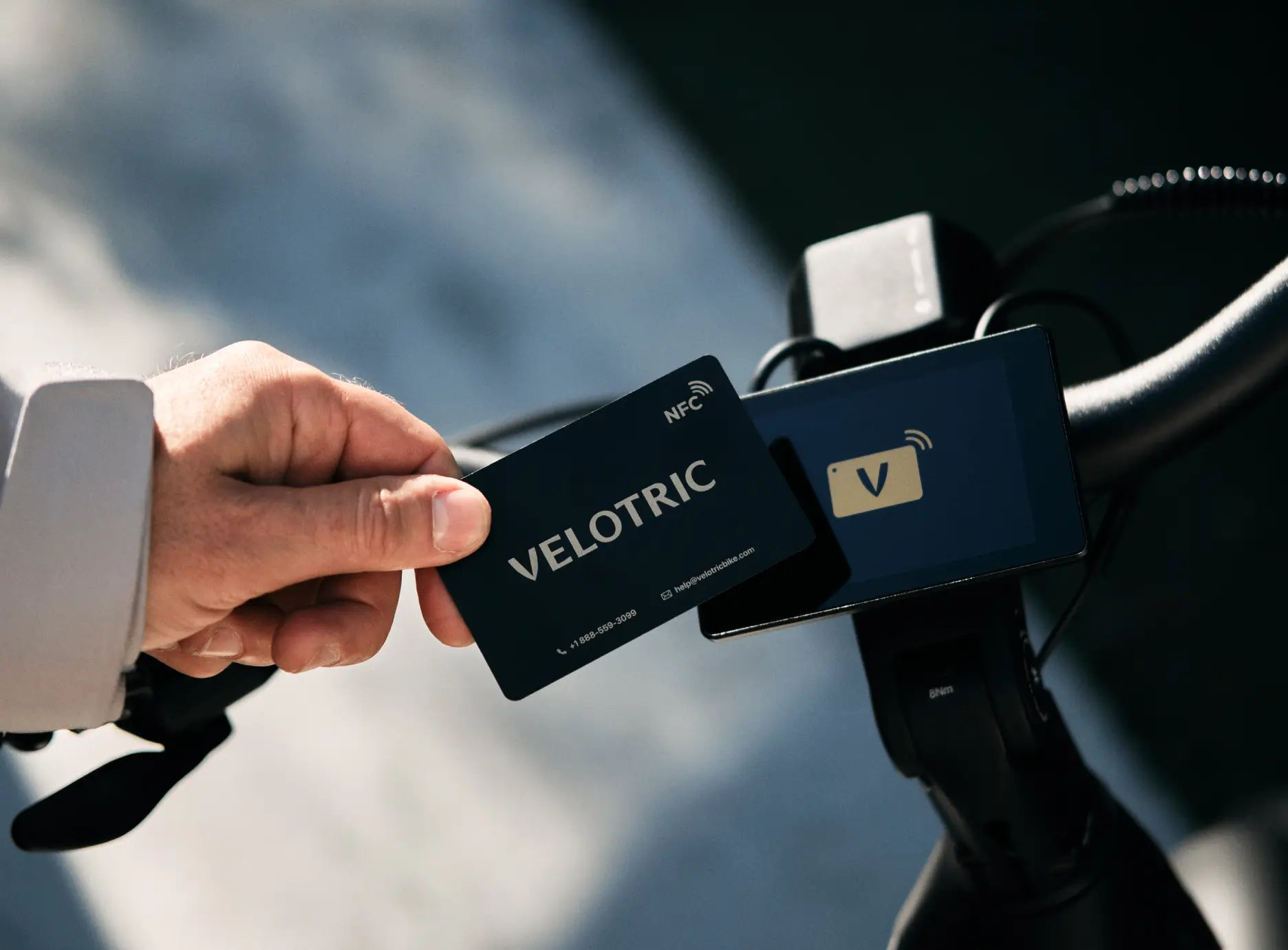 A person holds a VELOTRIC NFC card near the handlebar display of the Velotric Discover M, likely unlocking or activating this Velotric comfort commuter eBike electronically.